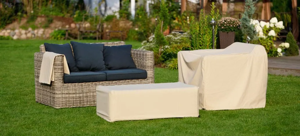Rattan-Lounge im Garten, Sessel und Hocker mit cremefarbenen Schutzhauben